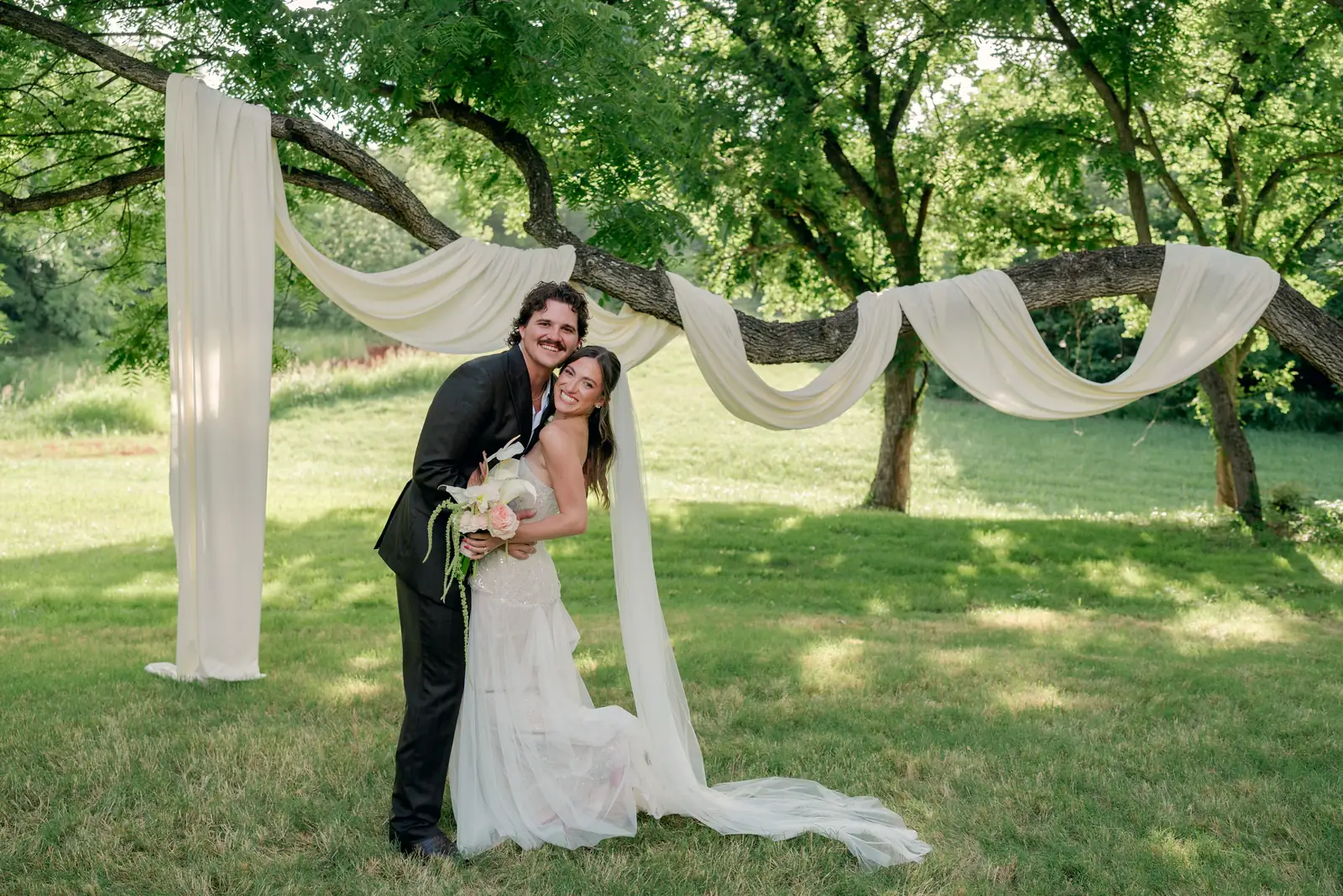 Rylee and Austin under ivory swags draped between the trees